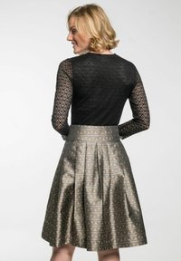 Schwarzes Spitzenoberteil mit langen Ärmeln und rundem Ausschnitt, kombiniert mit einem metallischen, plissierten Rock, der geometrische und florale Muster in bronzefarbenen Tönen aufweist.