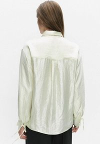 Licht crèmekleurig gestructureerd shirt met een kraag, lange mouwen en strikaccenten bij de manchetten. Lichtjes losse pasvorm, minimalistisch ontwerp.