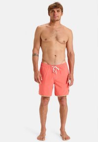 Calções de banho cor de coral com cintura elástica, cordão branco e acabamento amarelo. Tecido leve, comprimento acima do joelho, design simples.