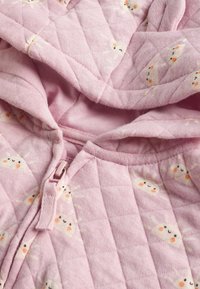 Tissu matelassé rose avec une fermeture éclair et des motifs de petits soleils souriants, partie d'un vêtement ou d'une couverture.