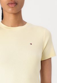 Light yellow cotton T-shirt with short sleeves and a round neckline, featuring a small embroidered logo on the upper left side.