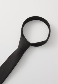 Crna kravata napravljena od teksturiranog materijala, s uskim oblikom i šiljastim završetkom. Kravata ima jednobojnu nijansu bez uzoraka.