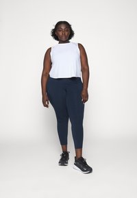 Top sin mangas de color gris claro con un escote redondo, combinado con leggings azul marino y zapatillas deportivas negras. Tela suave, corte relajado.
