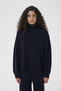 Marineblå turtleneck-genser laget av mykt materiale, med lange ermer og avslappet passform. Ribbet tekstur ved mansjetter og kant.