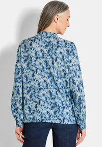 Fließende Bluse in Hellblau mit einem weißen und dunklerblauen abstrakten Muster. Sie verfügt über lange Ärmel mit elastischen Bündchen und einem rundem Halsausschnitt.