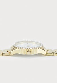 Montre en or avec un cadran blanc brillant, accents en perle autour de la lunette, côté texturé, et un bracelet à maillons.