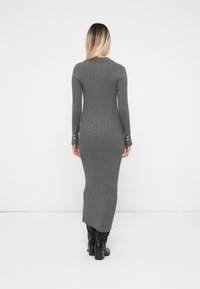 Μακρύ γκρι ριχτό φόρεμα με μακριά μανίκια, παρουσι�άζοντας εφαρμοστή σχεδίαση, ανοιχτές μανσέτες με κουμπιά και ευθεία σιλουέτα.