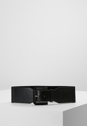 Ceinture large en cuir noir avec une grande boucle rectangulaire, présentée à plat sur une surface blanche contre un fond gris uni.