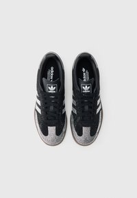 Černé tenisky Adidas se stříbrnými akcenty, texturovaným svrškem, bílými třemi pruhy a gumovou podrážkou. Navrženy s kulatou špičkou a zavazováním na tkaničky.