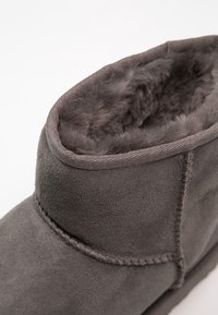 Harmaa mokkasiininen nilkkaboots, jossa on pehmeä turkisvuori, ommellut yksityiskohdat ja pyöristetty yläreuna. Pinnassa on sileä tekstuuri.