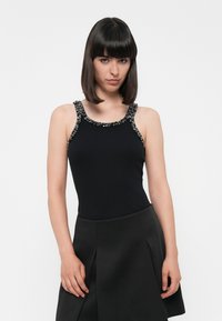 Top in raso nero a coste con spalline decorate, caratterizzato da un collo a barco. Abbinato a una gonna nera aderente con pieghe.