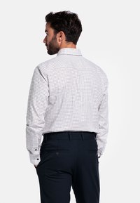 Witte geruite shirt met een puntig kraag, lange mouwen en knoopmanchetten; met contrasterende blauwe en rode ruitpatronen.