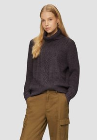 Dunkelvioletter gestrickter Pullover mit hohem Kragen und strukturiertem Zopfmuster, kombiniert mit khakifarbenen Cargo-Hosen mit Seitentaschen.
