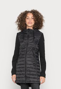 Gilet piumino nero con chiusura a zip e cappuccio, caratterizzato da un design trapuntato. Le maniche sono in tessuto nero, in contrasto con il corpo lucido.