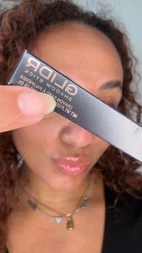 Personne aux cheveux bouclés tient près de la caméra une boîte noire de crayon pour ombre à paupières GLIDR, affichant le texte du produit clairement.