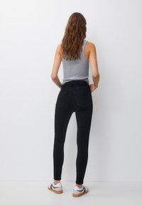 Jeans oscuros ajustados de mezclilla, con una cintura alta y bolsillos traseros. Combinados con una camiseta sin mangas gris y zapatillas blancas.
