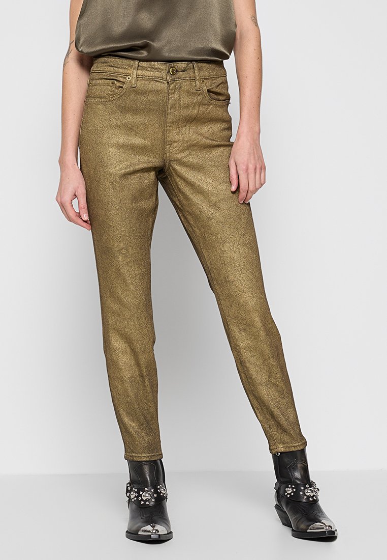 Złote metaliczne wąskie dżinsy o gładkiej teksturze i klasycznym pięciokieszeniowym kroju. Noszone z czarnymi, ozdobnymi botkami za kostkę.
