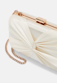 Pochette en satin crème avec motif en tissu torsadé, cadre en métal doré et bandoulière chaîne sur fond blanc.