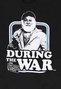 Sort t-shirt med grafik af en skægget mand i en frakke, der holder en pibe. Teksten lyder "UNDER KRIGEN" og "KUN TOSSE OG HESTE."