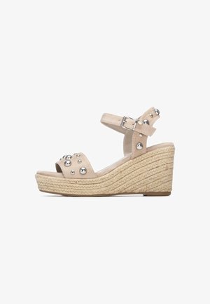 Sandalia de cuña beige con suela trenzada de yute, tiras de ante y detalles de bolas metálicas en la parte superior. Correa ajustable en el tobillo para un mejor ajuste.