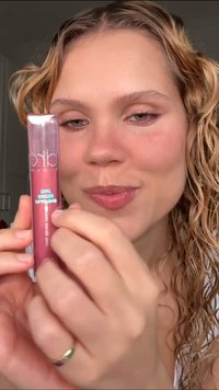 Gloss à lèvres dans un tube transparent avec une teinte rose brillante. L'applicateur est visible, avec une pointe arrondie pour une application en douceur.