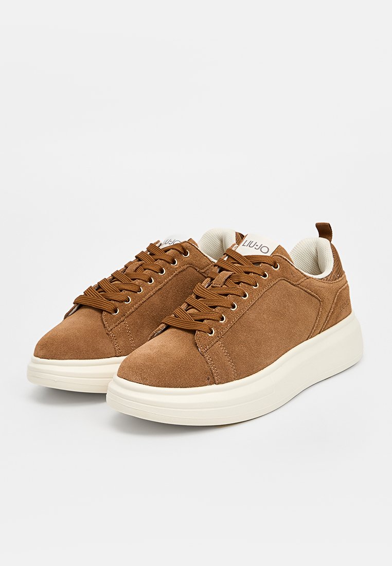 Sneaker in suede marrone con suole in gomma bianca, caratterizzate da un design con lacci e un accento del logo sulla linguetta. Texture liscia e forma arrotondata.