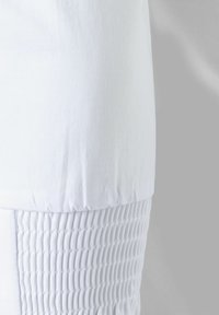 Witte kleding met een gladde stof aan de bovenkant en een textuur met plooien aan de onderkant. Naadlijnen zijn zichtbaar.