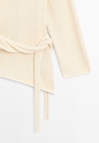 Manche de pull en tricot couleur crème avec une ceinture attachée nouée en nœud lâche d'un côté.