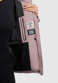 Ružová prešívaná bunda s čiernym vnútrom, na podšívke sú viditeľné dve štítky. Tkanina sa zdá byť hladká a ľahká.