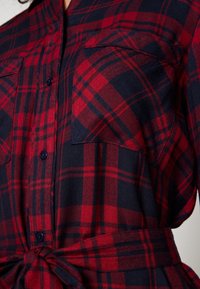 Rood en marineblauw geruite blouse met een knoopsluiting, beschikt over twee borstzakken, een gestrikt tailleband en textuurstof.