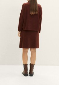Sada z hnědé pletené horní části a sukně, která má volný střih a texturovaný povrch, doplněná hnědými kotníkovými botami s robustní podrážkou.