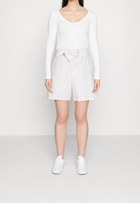 Shorts beige clair avec un détail de nœud à la taille. Associés à un haut à manches longues blanc et des baskets blanches. Texture lisse, coupe décontractée.