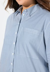Skjorta med knappar i ljusblå och vita ränder. Har en bröstficka och en klassisk krage. Mjuk, strukturerad tyg med avslappnad passform.