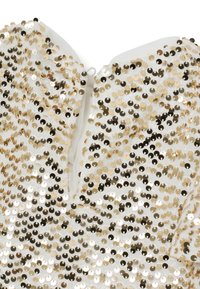 Top en sequins dorés et argentés avec une surface texturée, présentant une fermeture éclair au dos et une base en tissu blanc uni.