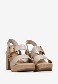 Sandali platform beige con cinturini larghi e una grande fibbia rettangolare. Realizzati in materiale testurizzato con un tacco simile al legno.