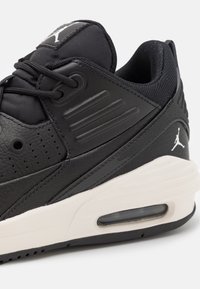 Czarny sportowy but z fakturowanej skóry i siateczki. Posiada białe logo, wyściełany kołnierz oraz widoczną poduszkę powietrzną w podeszwie.