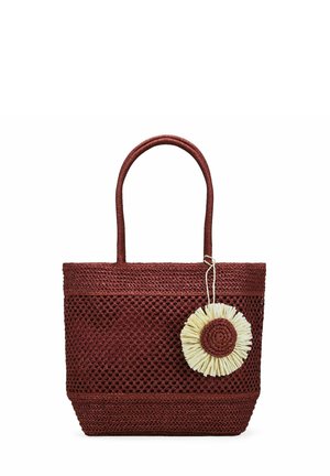 Bolsa tote tejida de color rojo oscuro con dos asas y un adorno decorativo redondo en crema y rojo colgando en un lado.