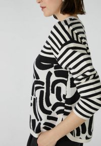Zwart-wit sweater met abstracte patronen op de voorkant en gestreepte mouwen, gemaakt van zacht materiaal met een relaxte fit en zijsplitten.