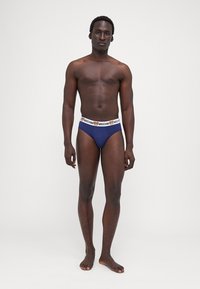 Navy blue men's briefs made of soft fabric, featuring a white elastic waistband with a logo print. Simple design and snug fit.
