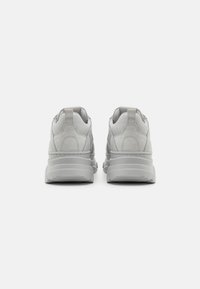 Grijze sneakers met een glad synthetisch bovenwerk en getextureerde accenten, voorzien van een dikke rubberen zool en een gepolsterde hiel voor comfort.