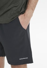 Svarta atletiska shorts med en slät yta, som har sidofickor och en vit "ENDURANCE"-logotyp vid den nedre fållen.