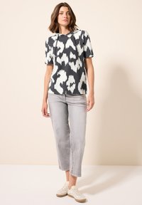 Sudadera de manga corta en estampado ikat en blanco y negro, con capucha ajustable. Combinada con jeans recortados en gris claro y zapatillas blancas.