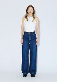 Jeans a gamba larga blu scuro in denim con vita alta, abbinati a un top bianco attillato. Tessuto liscio e design classico a cinque tasche.