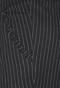 Svart tyg med vertikala vita räfflor; har volangdetaljer vid midjan; mjuk textur; figurnära design.