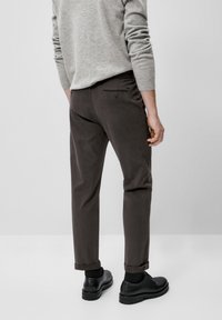 Maglione grigio abbinato a pantaloni marrone scuro. I pantaloni hanno un risvolto e una tasca posteriore con bottone. Scarpe nere completano il look.