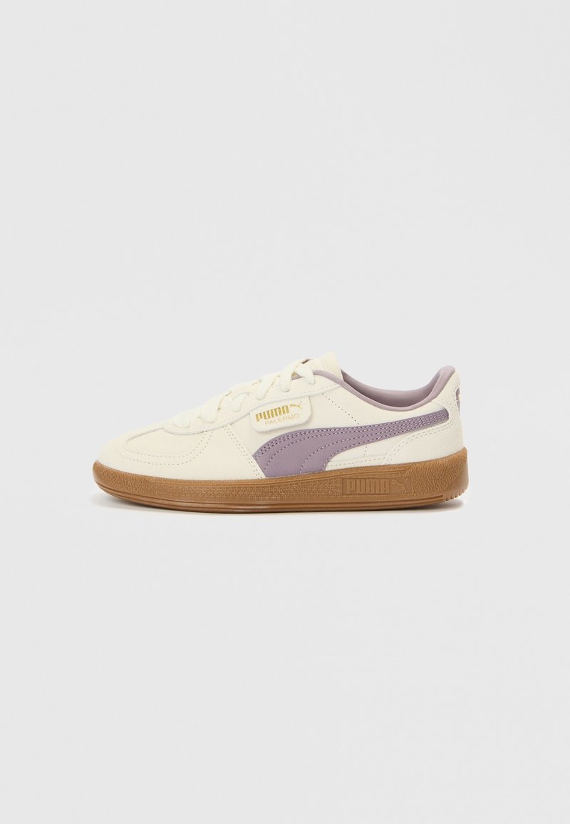 Baskets blanches Puma avec bande latérale violette et semelle en gomme, montrées de profil extérieur sur un fond clair uni.