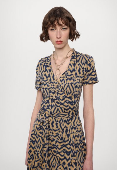 Abito senza maniche in beige con motivi geometrici blu navy, scollatura a V e vita aderente, con una leggera drappeggiatura nella gonna.