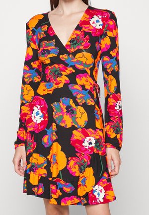 Kvinde iført en sort slå-om kjole med lange ærmer med store lyse orange, pink, røde og blå blomsterprint.