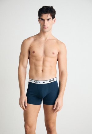 Boxers ajustados Nike azul marino con una cinturilla blanca y marcada con la marca, que presentan un diseño entallado y una textura suave. El modelo posa con el torso desnudo.