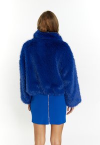 Blauwe nepbontjas met hoge kraag en wijde mouwen, cropped ontwerp. Draag een blauwe aansluitende mini rok met een centrale rits.
